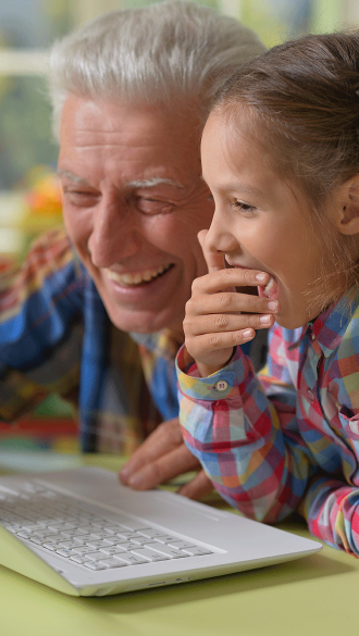 Grandfather with granddaughter looking at laptop laughing having fun