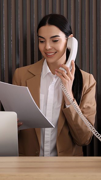 Hero-Receptionist-with-papers-talking-on-phone-at-countertop-in-hotel