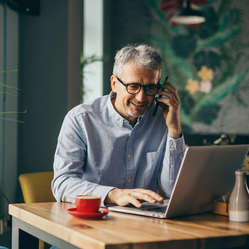 Senior man on mobile phone and laptop at home using Wi-Fi