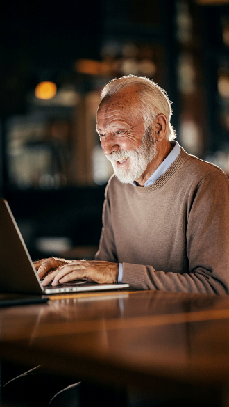 Senior man on laptop at night in home using Wi-Fi